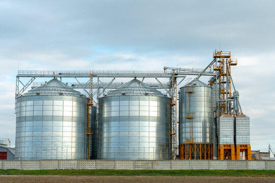A large modern plant for the storage and processing of grain crops. view of the granary on a sunny day. Large iron barrels of grain. silver silos on agro manufacturing plant for processing and drying