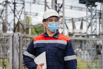 An electrical substation engineer inspects modern high-voltage equipment in a mask at the time of pondemia. Energy. Industry