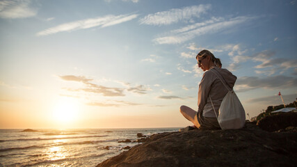 A young woman sitting on the rocky Atlantic coast during sunset