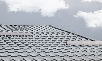 Roof of a house made of gray metal slate against the sky with clouds
