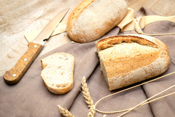 loaf of fresh crisp bread and cutted slice of baguette on wooden background with knife and copy space, baked pastry food closeup