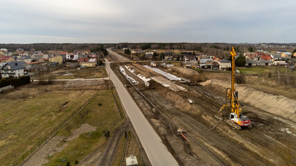 Railway works in small village. Railroad construction and modernisation site. Aerial view on excavator and railway track components. 