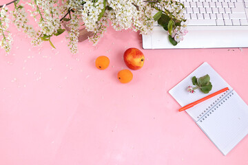 Work desk of a modern woman, home office. Computer, notepad, spring flowers, peaches on a light table. Minimal business concept, healthy lifestyle, flat lay, place for text.