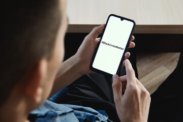 The businessman holds a mobile phone in his left hand and looks at a screen with the text Black Lives Matter. The concept of racism of black people in the world