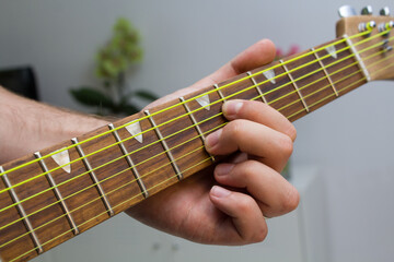 Man hands playing chords on electric guitar with yellow strings with white background.