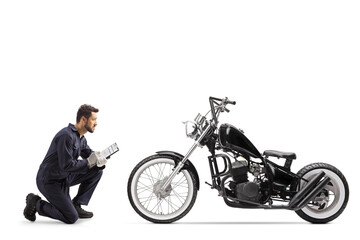 Obraz na płótnie Canvas Motorbike mechanic in a uniform kneeling and looking at a chopper and writing a document