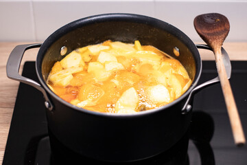 Homemade apricot jam, boling in a black pot with a wooden spoon on the side. Preparing seasonal...