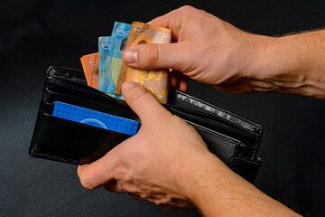 Man hand pulling money from wallet, black background and black wallet.