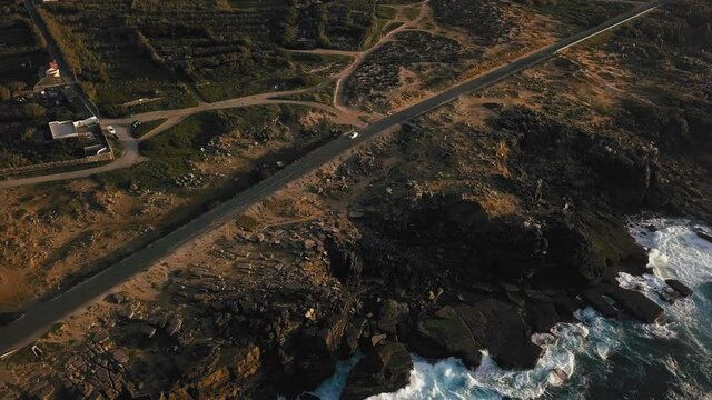 Stunning cinematic aerial view following car in motion through coastal road in top down birdseye view mode.