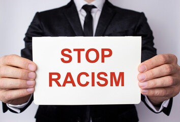A man holds a white sheet of paper with the message in red letters STOP RACISM.
