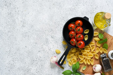Raw pasta - Conchiglie with spices, tomatoes and basil on a concrete background. Top view.
