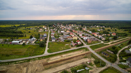 Fototapeta na wymiar Aerial view on small village located in central Poland. Summer landscape, cloudy afternoon. Green meadows, calm light. Small detached houses, streets, railroad.