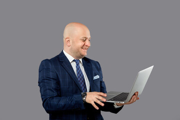 A happy bald man with a laptop in his hands smiles and looks at the screen.