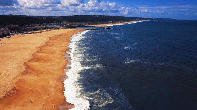 Flying over a sandy beach. Waves break on a sandy beach on the Atlantic coast, aerial View. Nazare, Portugal.