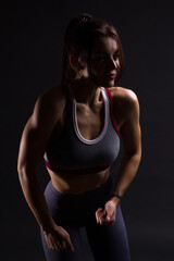 Obraz na płótnie Canvas Fitness young woman in training clothes, dark backlit photo