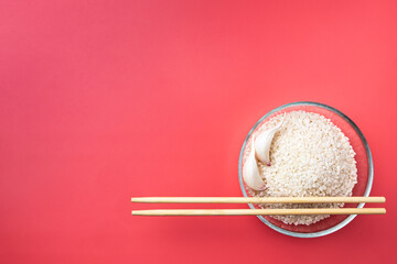 Flat lay. A transparent glass bowl with rice, garlic and chopsticks on a pink background. Traditional ingredients and symbols of Asian cuisine. The concept of food minimalism. Copy space.