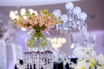 A bouquet of beautiful peach flowers in a round vase on a crystal stand in the concept of wedding decor. Spring flowers.