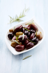 Green and Kalamata olives with fresh rosemary on bright wooden background. Close up. 