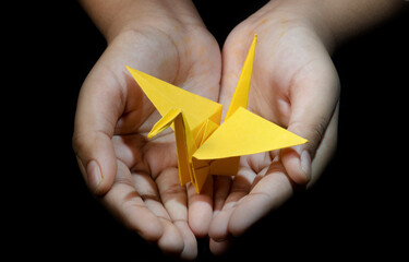 Hand holding Origami Paper Crane (Orizuru), Yellowbird.  on Black Background  - Powered by Adobe