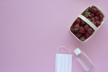Medical face mask, sanitizer and strawberries on a pink background. Summer coronavirus crisis composition. Flat lay, copy space.