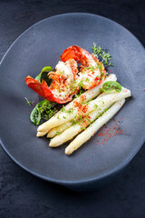 Traditional barbecue spiny lobster tail sliced and offered with white asparagus and lettuce as top view on a modern design plate