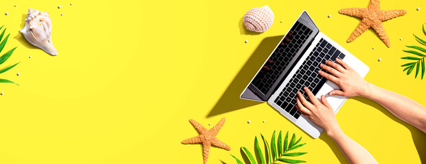 Person using a laptop computer with summer theme objects - flat lay