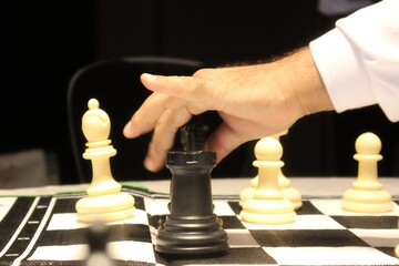 A person's hand moving the black king in a chess game competition indoors