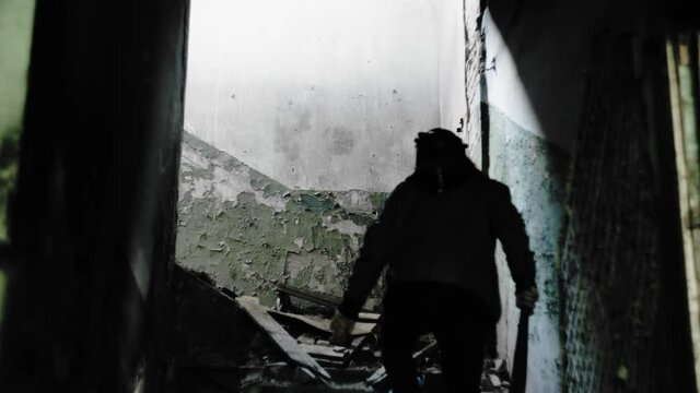 The guy goes up the stairs of the old house. The guy is wearing a hard hat and a bat in his hands.