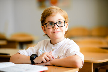 cute blonde school student with stylish glasses writing in classroom