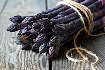 Fresh bunch of purple asparagus on a wooden background.
