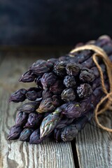 Fresh bunch of purple asparagus on a wooden background.
