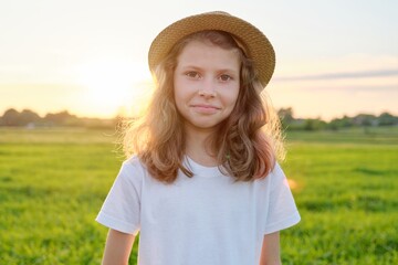 Portrait girl child 9, 10 years old in hat, summer green meadow sunset background