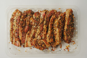 Fresh pork belly slices in Korean style marinate and herbs on a plastic tray on simple table cloth.