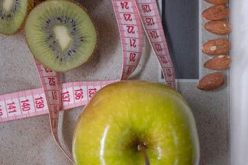 Red measuring tape, apple, kiwi and almonds on beige bathroom scales. Diet and Healthy life, loss weight, sport concept. Top view. Copy space. Isolated. White background