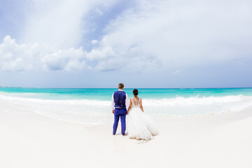 Newlyweds holding hands hugging at white sandy tropical caribbean beach landscape after wedding ceremony of marriage on destination wedding honeymoon travel looking on blue sea in Punta Cana Dominican