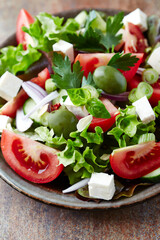 Healthy salad with feta cheese, green olives and tomatoes. Rustic stone background. Close up.	