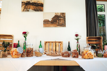 Salty bar of several kinds of nuts, potato chips, salted pretzels, sticks and snacks decorated on wooden table inside room. Wedding or party concept.