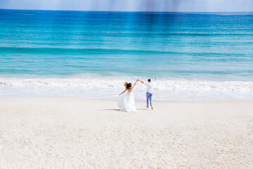 Fototapeta na wymiar Newlyweds holding hands hugging at white sandy tropical caribbean beach landscape after wedding ceremony of marriage on destination wedding honeymoon travel looking on blue sea in Punta Cana Dominican