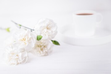 White cup of black coffee and carnations flowers on a white background, copy space