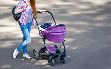 Young stylish mother walking with baby stroller. Mom walks with stroller. Young stylish mother enjoys walking with her newborn, baby sleeping in pram.
