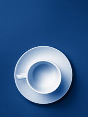 Flat lay. Empty white cup on a saucer on a blue background. Trend color. Classic blue. Copy space. 