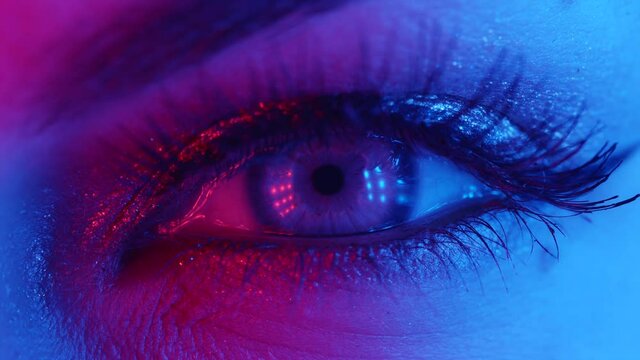 Extreme close up of human eye iris under neon light 4K. Female with beautiful makeup, glitter shadows and false lashes. Womens green eye contracting. Nightlife, night club concept.