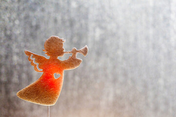 Silhouette of a Christmas angel with a trumpet and a burning heart on a bright silver background;...