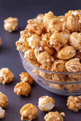 Sweet caramel popcorn in glass bowl. Close up. Dark grey background.