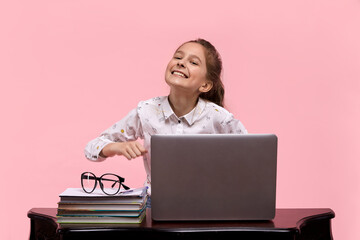 A young girl smiles on a pink background sitting at a laptop