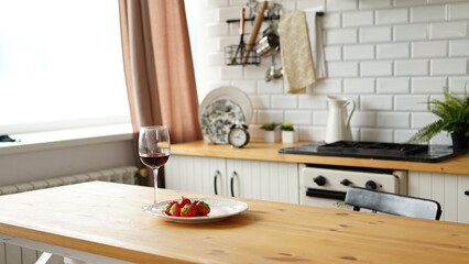 Close up of glass of wine with strawberries on plate on table in kitchen. Concept of dating.