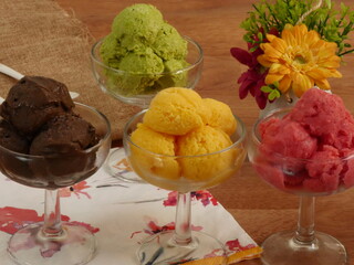 Sélection de saveurs gourmandes de glacesaux couleurs vives servies dans des tasses  individuelles sur une  table en bois rustique dans un glacier.