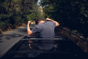 Young happy man drives a car and holds his hand out from the window. Driver enjoys driving and shows Ok sign with his hand out of window. Road trip, travel and freedom concept.