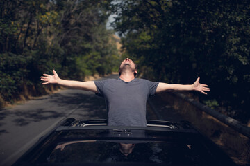 Young happy man drives a car and holds his hand out from the window. Driver enjoys driving and shows Ok sign with his hand out of window. Road trip, travel and freedom concept.