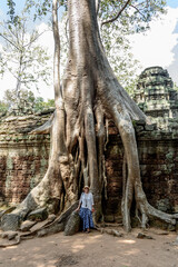 Fototapeta na wymiar Caucasian Woman Posing Next to a Huge Ficus Tree Roots Covering Walls at Ta Prohm Temple at Angkor Wat Siem Reap Cambodia